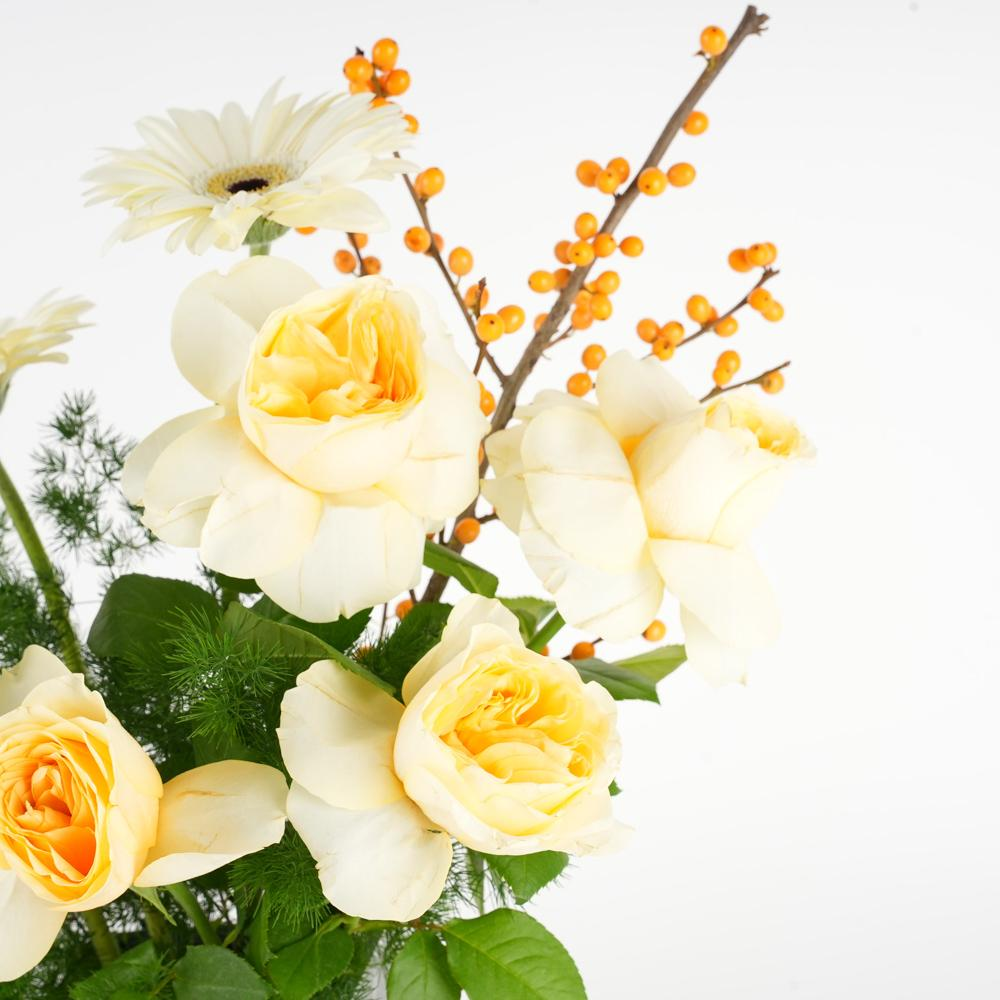 An arrangement of yellow roses, leaves, and other additions