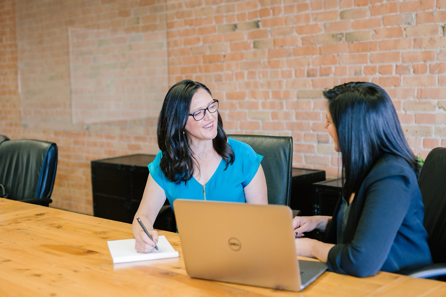 Two businesswomen sitting at a conference table, engaged in conversation.