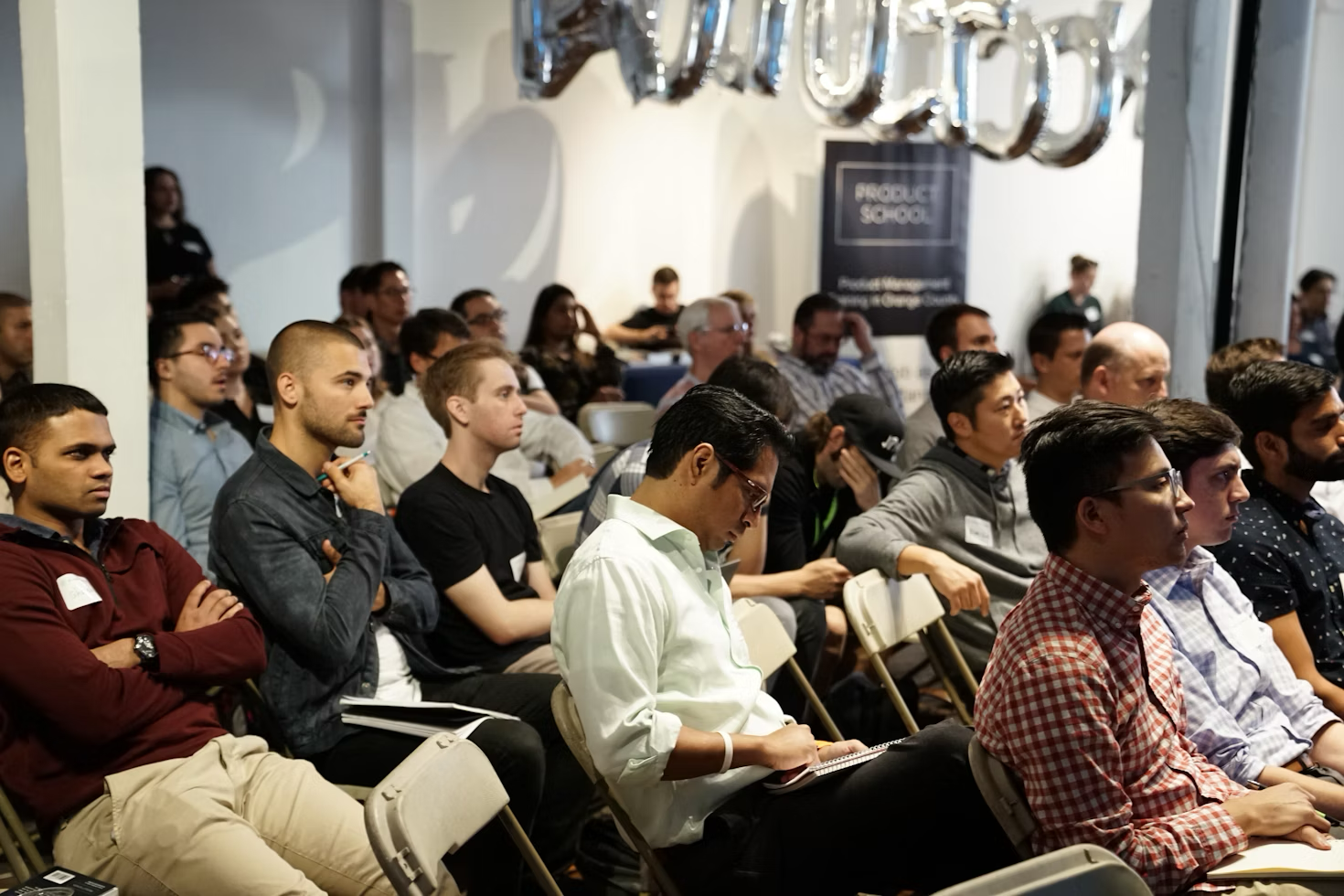 A group of diverse people sitting in a conference room, listening to a presentation.