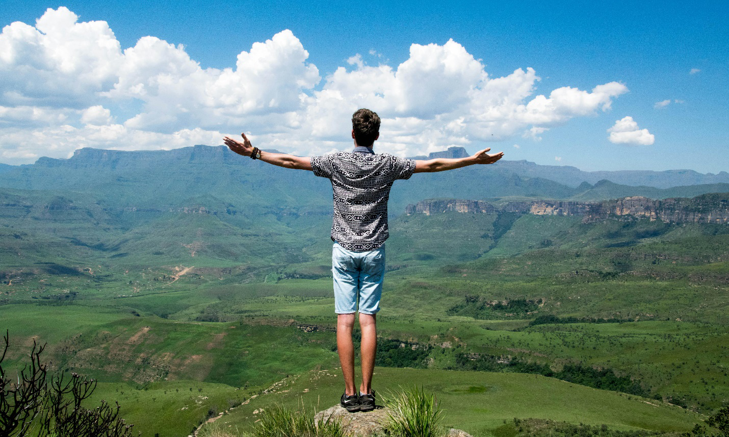 The back of a man standing on a rock overlooking a mountainous view and big clouds